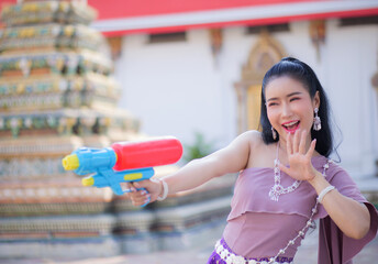 Portrait cheerful young asian woman holding plastic water gun Smiling and having fun playing in the water Songkran festival, Thailand. isolated on pink background. Thai New Year's Day.