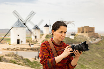 Young woman tourist with a camera Consuegra, who came to the Mota del cuervo, photographs the surroundings, standing near the ..windmills - 769228516