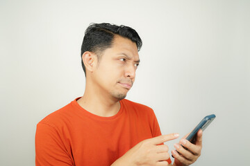 Asian man in orange t-shirt feeling sad and depressed looking at smartphone on isolated background