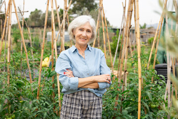 Happy elderly woman posing in her garden, in the backyard of a village house - 769231102