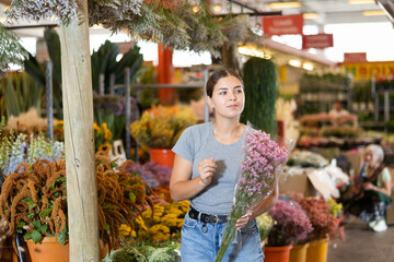 Smiling interested young girl buying bouquet of colorful fresh flowers at market - 769231343