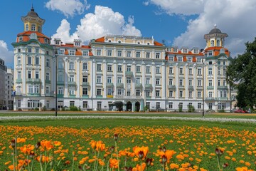 Fototapeta premium A grand white building stands tall as vibrant orange flowers bloom in front, creating a picturesque scene of contrast and beauty
