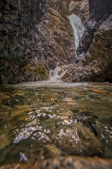 Majestic waterfall rushing down amid the high, textured rocks into the rocky riverbed below