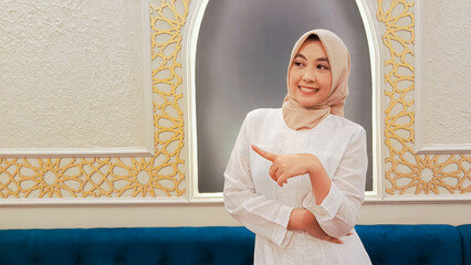 elegance of indonesia woman wearing hijab candid cheerful smile expression, hand pointing to the...