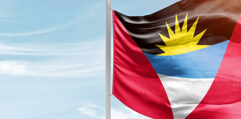 Antigua and Barbuda national flag with mast at light blue sky.