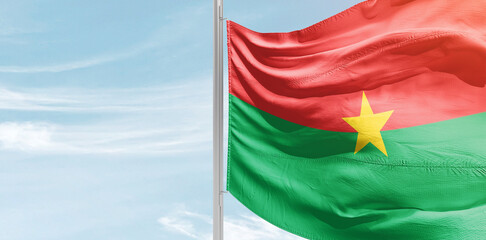 Burkina Faso national flag with mast at light blue sky. - obrazy, fototapety, plakaty