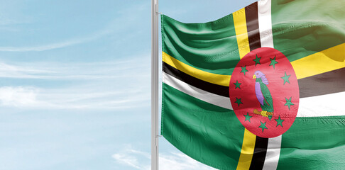 Dominica national flag with mast at light blue sky.