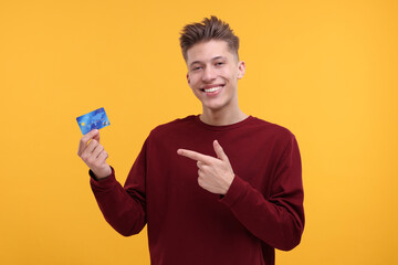 Happy man pointing at credit card on yellow background
