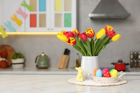 Easter decorations. Bouquet of tulips, painted eggs and bunny figure on table indoors. Space for text
