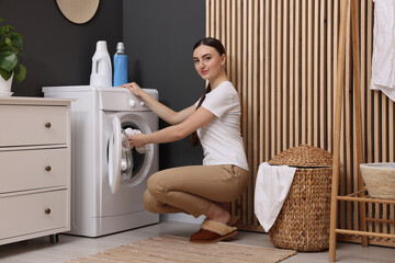 Beautiful woman putting shirt into washing machine in laundry room
