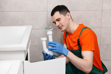 Smiling plumber wearing protective gloves repairing sink in bathroom