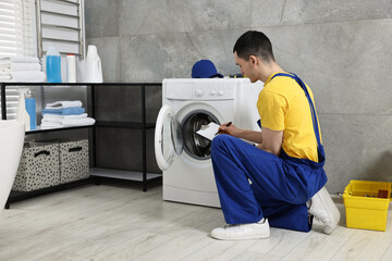 Young plumber writing results of examining washing machine in bathroom