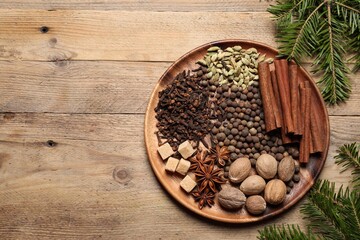 Different spices, nuts and fir branches on wooden table, flat lay. Space for text
