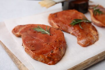 Board with raw marinated meat and rosemary on light table, closeup