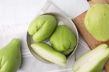 Cut and whole chayote in bowl on white tiled table, flat lay