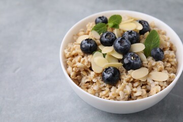 Tasty oatmeal with blueberries, mint and almond petals in bowl on grey table. Space for text