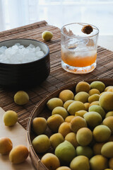 Fresh plums, rock sugar and plum wine in a clear glass on a wooden table. Ingredients for making plum wine or Umeshu and plum syrup. Selective focus at plum wine.