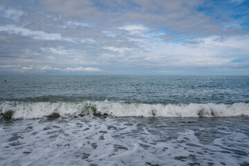 An incoming wave on the Black Sea and a pebble beach on the Sochi coast on a sunny summer day with clouds, Sochi, Krasnodar Territory, Russia