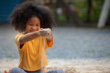 Little African girl slowly lets sand slip through her hands onto the ground, summer outdoor...