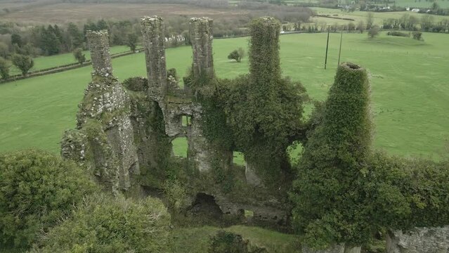 Carbury castle ruins covered in green ivy, in kildare, ireland, with lush fields around, aerial view