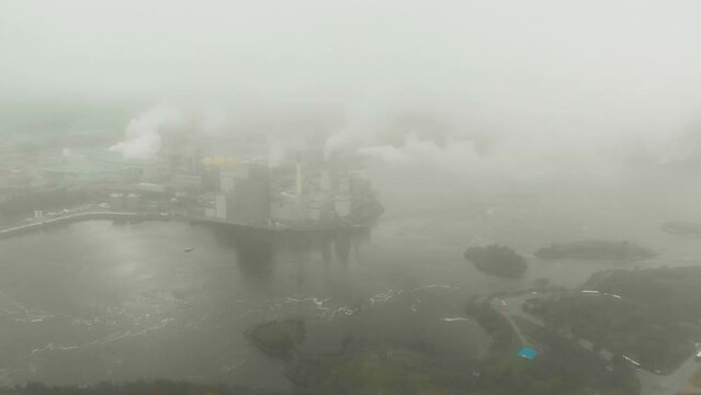 Aerial shot emerging from the thick clouds to reveal the Irving Pulp and Paper plant next to the reversing falls as it shoots toxic smoke into the air.