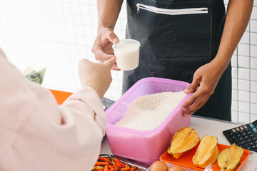 Seller wear apron helping customer to weighing rice with plastic measure cup