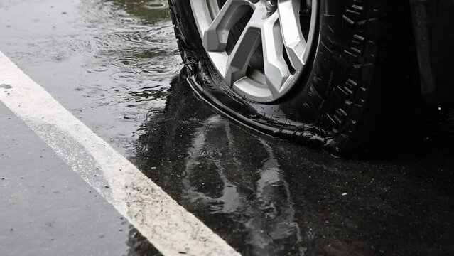 pouring rain on a silver car wheel with a flat deflated black tire in a white parking paint line and a reflection off of the water STATIC SHOT 60fps