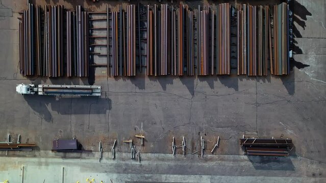 Drone top down overview of semi truck transporting steel beams across industrial yard, ascend