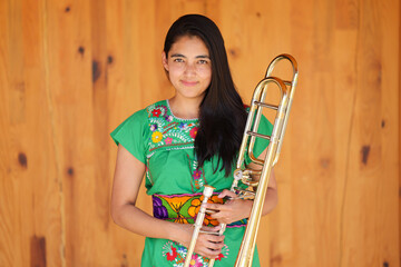 young mexican indigenous woman smiling in traditional dress holding trombone