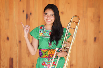 young mexican indigenous woman smiling and pointing in traditional dress holding trombone
