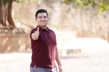 portrait of young mexican man smiling with thumbs up with blurred background