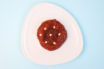Large red velvet cookie with nuts on white plate isolated over blue background