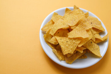 Tortilla or Nacho chips for snack on white plate over yellow background, top view, copy space.