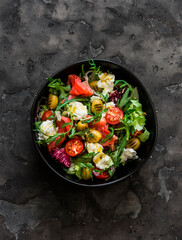 Delicious salad with vegetables, lightly salted salmon, olives, mozzarella on a dark background, top view