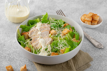 Caesar salad with lettuce, grilled chicken breast, parmesan cheese and croutons in a bowl on a gray concrete background. Copy space