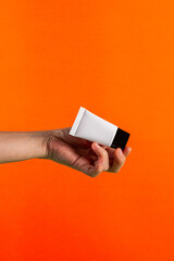 Plastic white tube for cream or lotion. Skin care or sunscreen cosmetic in hand on orange background.