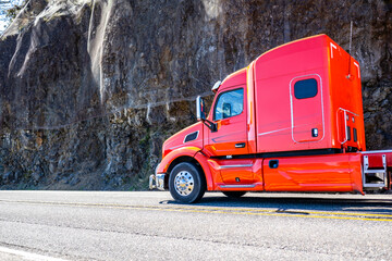 Bright red big rig semi truck with extended cab transporting cargo driving on the mountain road...