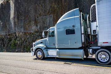 Gray powerful high cab big rig semi-truck transporting frozen cargo in refrigerator semi trailer...