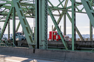 Powerful tow big rig semi truck towing red classic broken semi truck driving on the truss arched bridge