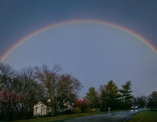 Suburban Midwestern street on rainy evening in early spring  with  rainbow in the sky; driving car at distance