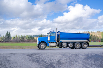 Profile of the blue big rig tip truck with two tipper trailers running on the construction side for the next load