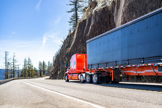 Professional carrier red big rig semi truck transporting cargo in tarp covered dry van semi trailer running on the mountain winding road