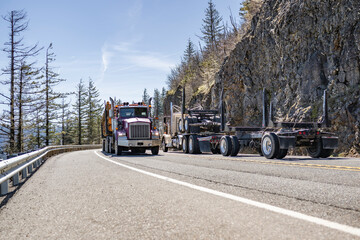 Two tree log carrier big rig semi trucks with semi trailers met on a mountain road moving towards each other
