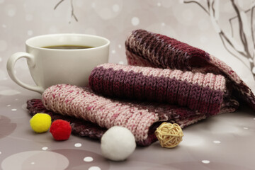 A cup of coffee and a warm knitted scarf. Hot coffee and a scarf provide warmth during the cold season. Cozy atmosphere in the form of a cup of coffee and a scarf.