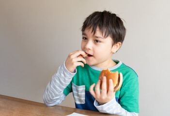 Preschool kid boy eating hamburger sitting in nursery cafe,Cute happy boy eating chicken burger for...