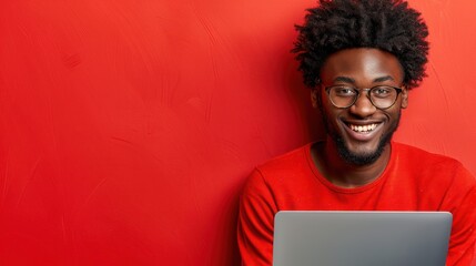 A man wearing glasses and a red shirt is actively using a laptop - Powered by Adobe