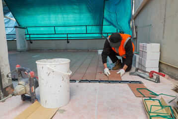 Worker is laying new tiles for the construction of a flooring over insulating material. Renovation of the flooring of a terrace which also functions as a roof