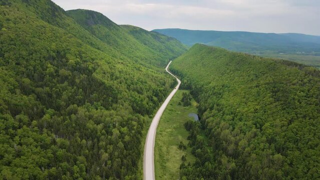 Drone shot of a stunning scenery of the famous Cabot Trail with a huge mountain range with a road going straight through the middle located on Cape Breton Island, Nova Scotia in Canada shot in 4k.