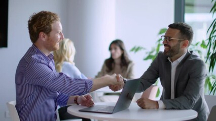 Two professionals shake hands, concluding a meeting as colleagues observe