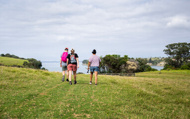 Three people walking on green meadows at Shakespear Regional Park. Auckland Region.